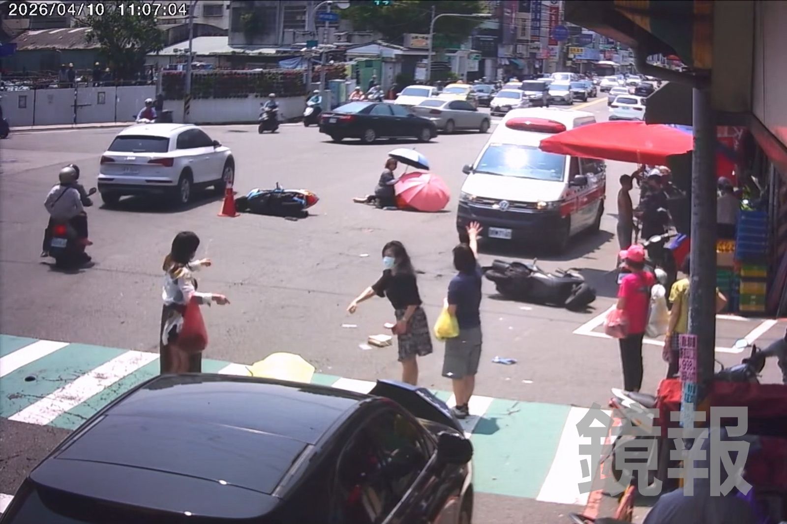 2名機車騎士遭撞倒地，民眾趕緊拿著傘幫忙遮蔽烈陽，並揮手示意救護車趕快過來救援。民眾提供