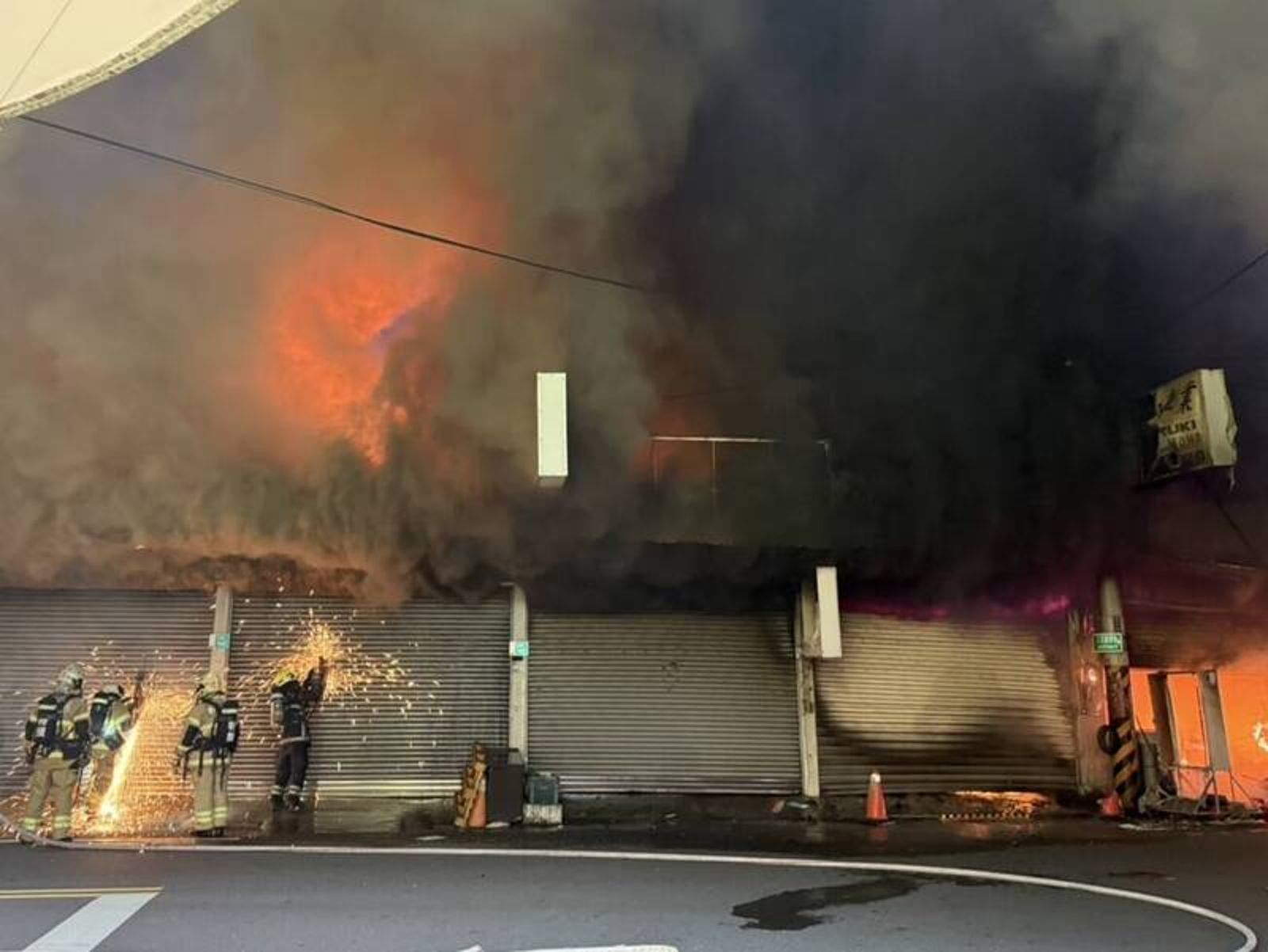 消防員試圖鋸開鐵捲門，以利撲滅火源。讀者提供