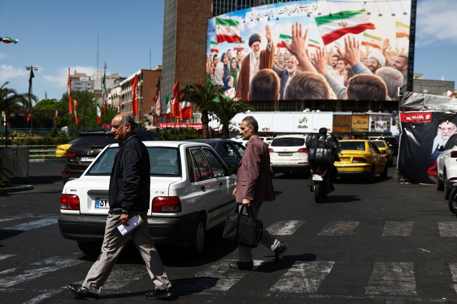 4月11日，伊朗德黑蘭，民眾走過建築上展示已故最高領袖哈梅內伊畫像的看板。圖／東方IC