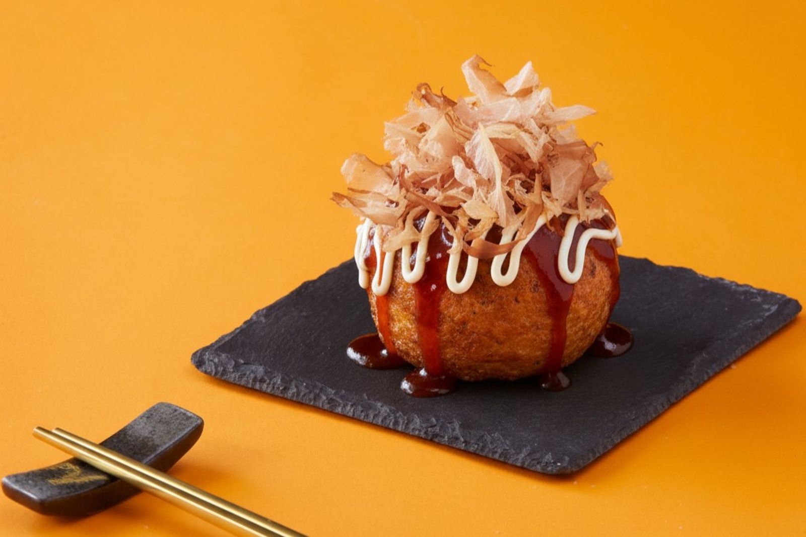 「東泉辣醬巨無霸章魚燒」外酥內嫩，內餡有章魚、蛤蜊、天婦羅碎、玉米與蔬菜，再淋上東泉辣醬與花生醬，鹹香微辣又帶濃郁花生風味。（198元／顆，爆彈燒本舖供圖）