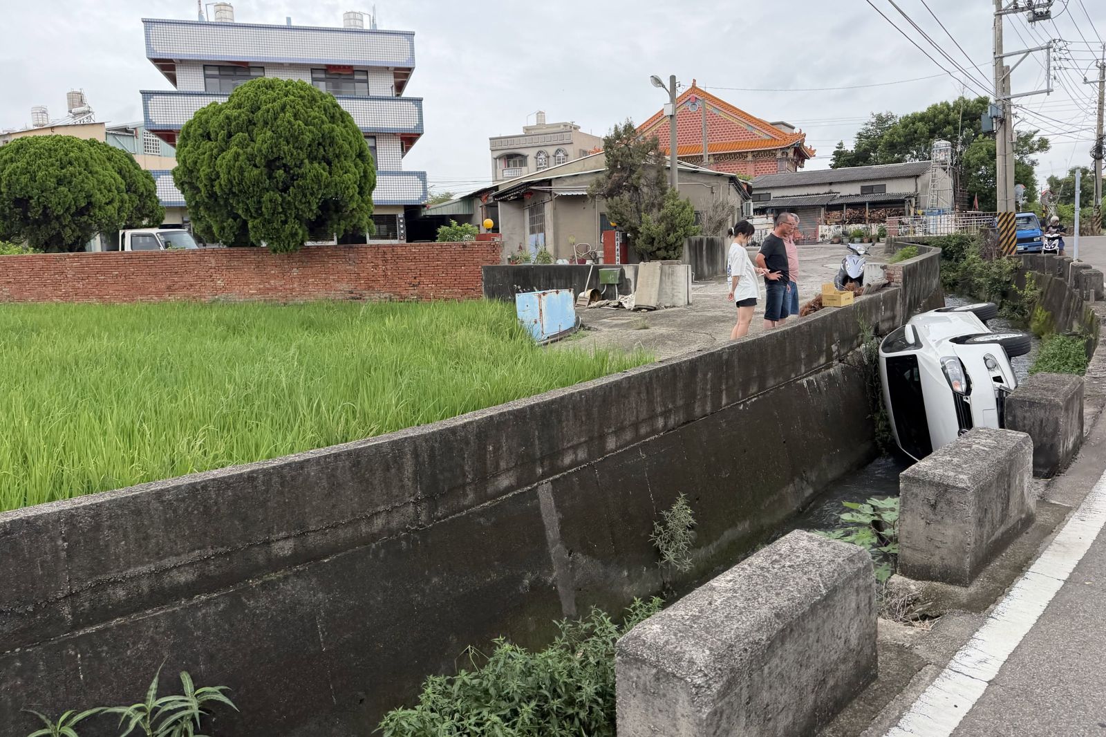白色轎車翻落排水溝,引發附近民眾關切,所幸母子3人及時脫困,送醫無礙。圖/畫面授權threads bob_kuei