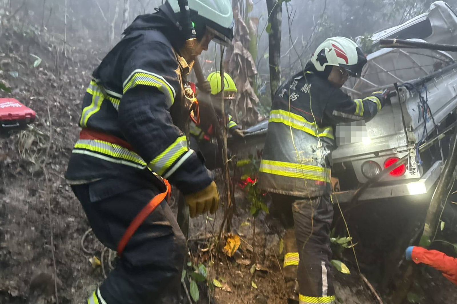 小貨車翻覆在山谷邊坡，車體嚴重變形，搜救隊員進行破壞，協助患者脫困。民眾提供