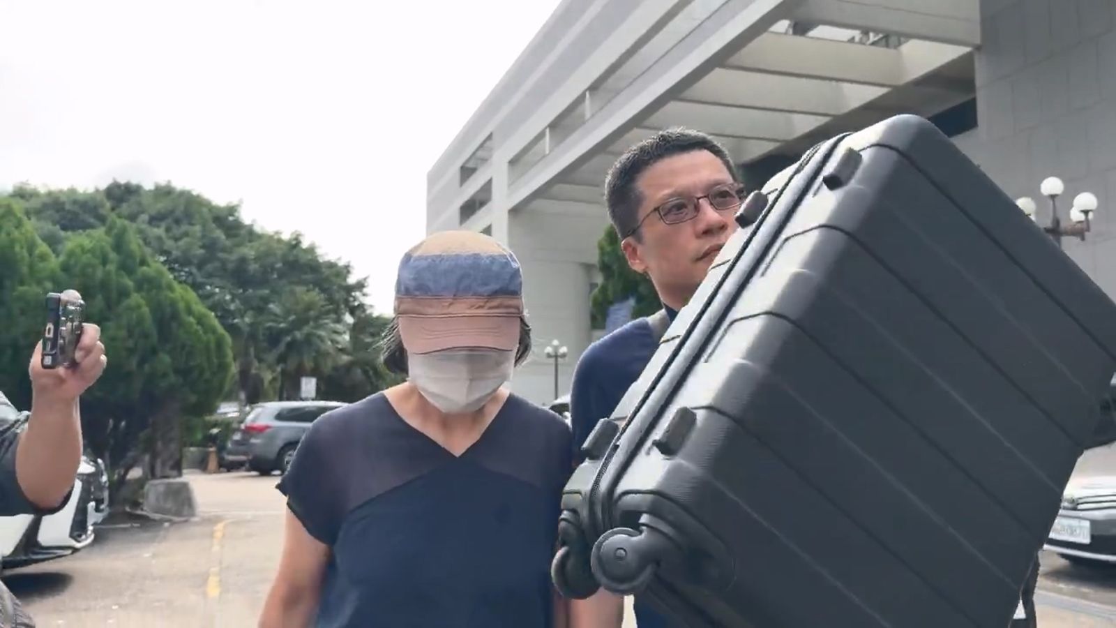 泰山企業前任總經理沈怡君(左)獲裁定交保，隨行男子頻頻用行李箱擋鏡頭。圖／民眾提供